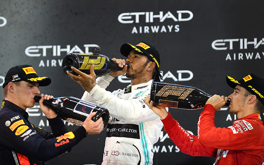 表彰台の上でシャンパンを飲むルイス・ハミルトンとマックス・フェルスタッペンとシャルル・ルクレール、2019年F1アブダビGPにて