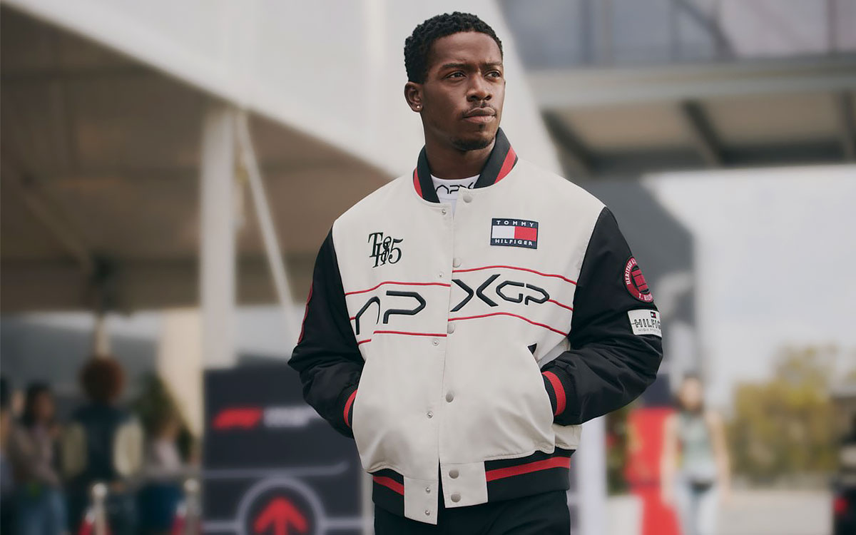 『F1 MOVIE SATIN VARSITY JACKET(税込110,000円)』を着用するジョシュア・ピアース演じるダムソン・イドリス、映画『F1:The Movie(邦題:F1/エフワン)』とトミー ヒルフィガーがコラボした「APXGP」コレクション